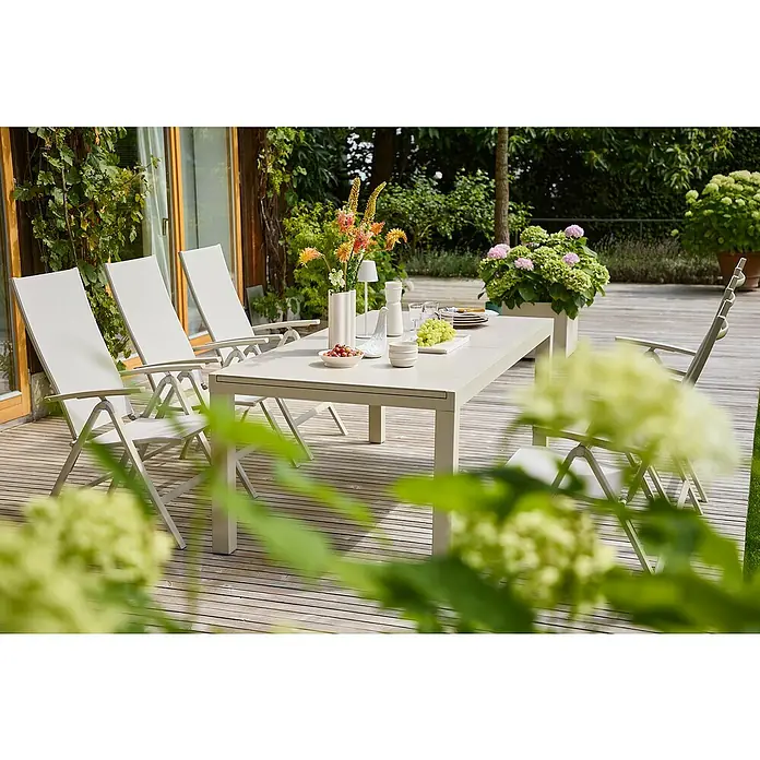 Sunfun Maja Sillón de posiciones - Aluminio, Respaldo regulable, Beige, An x Pr x Al: 61 x 68 x 110 cm - Un juego de mesa de jardín con cuatro sillas en una terraza de madera rodeada de exuberante vegetación ofrece una escena idílica.