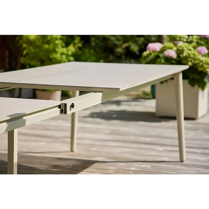 Sunfun Solo Gartentisch - L x B x H: 230 x 100 x 76,5 cm, Aluminium, Sintered Stone, Light-Greige, Ausziehbar - Nahaufnahme eines ausziehbaren Gartentisches mit Metallrahmen und sanfter Farbpalette auf einer Terrasse, umgeben von üppigem Grün.