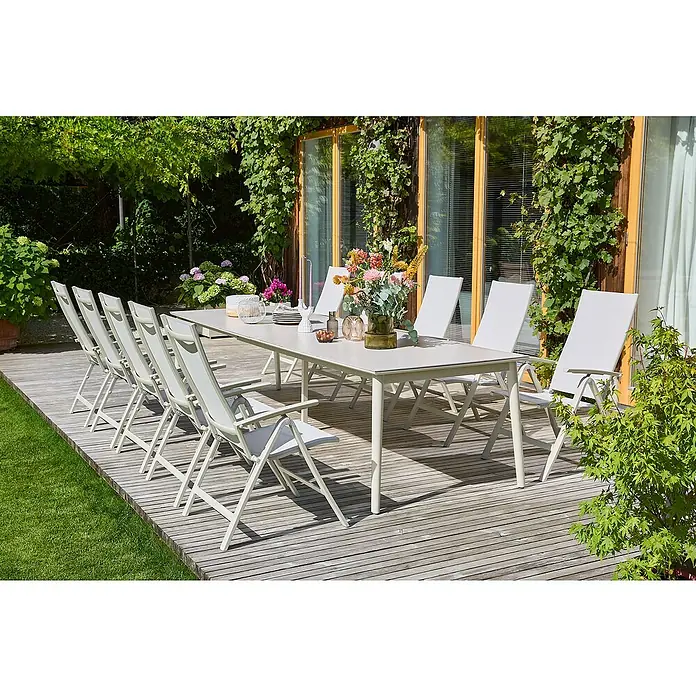 Sunfun Solo Garten-Tischplatte Erweiterung - L x B: 60 x 100 cm, Aluminium, Sintered Stone, Light-Greige - Ein langer Esstisch mit zehn weißen Stühlen im Freien, dekoriert mit Blumen und Geschirr, umgeben von Grün.