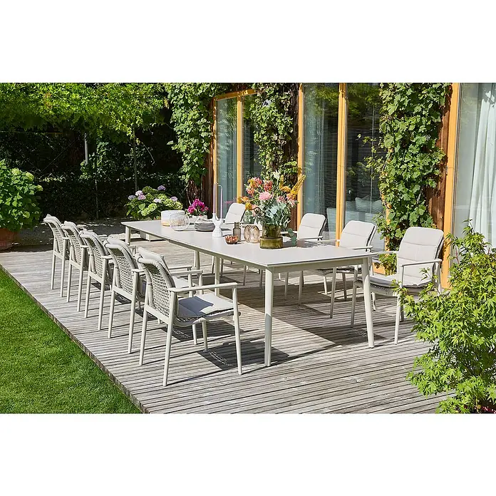 Sunfun Gartenmöbel-Set Solo Rope - 22 -tlg., Aluminium/Sintered Stone/Kunststoff/Olefin, Light-Greige, Ausziehbar - Gartenszene mit einem langen Esstisch und passenden Stühlen auf einer Holzterrasse, umgeben von üppigem Grün.