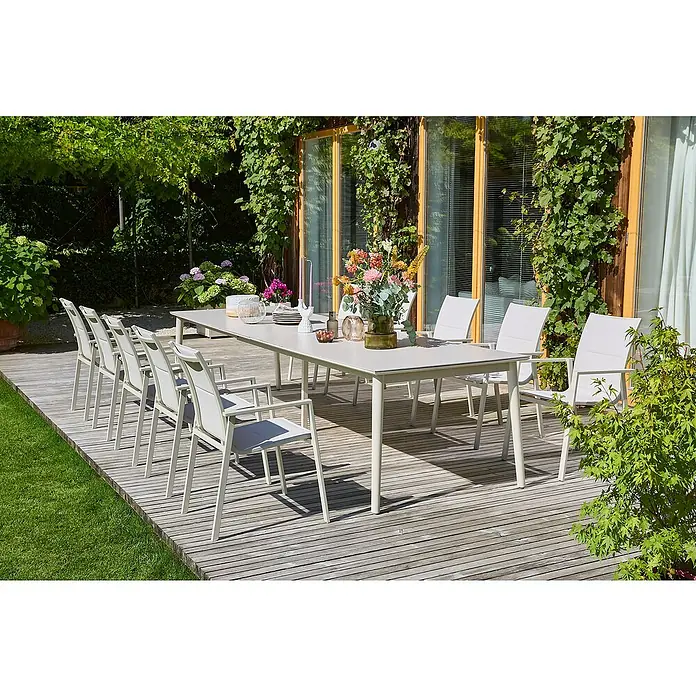 Sunfun Gartenmöbel-Set Solo Rope - 12 -tlg., Aluminium/Sintered Stone/Textilen, Light-Greige - Ein langer Esstisch mit Stühlen im Freien, ideal für Mahlzeiten im Garten oder auf der Terrasse, umgeben von Grünpflanzen.