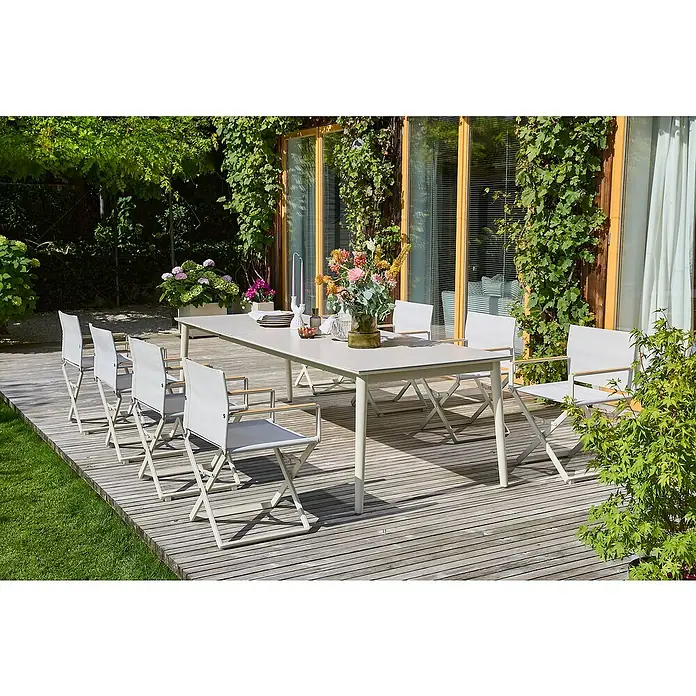Sunfun Gartenmöbel-Set Solo - 9 -tlg., Aluminium/Sintered Stone/Textilen, Light-Greige, Ausziehbar - Ein Gartentisch mit weißen Stühlen auf einer Terrasse. Der Tisch ist mit Blumen und Geschirr gedeckt und lädt zum Verweilen ein.