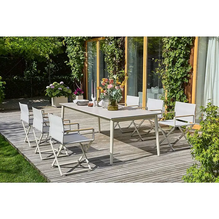 Sunfun Gartenmöbel-Set Solo - 7 -tlg., Aluminium/Sintered Stone/Textilen, Light-Greige, Ausziehbar - Ein Gartentisch-Set mit weißen Klappstühlen auf einer Holzterrasse. Das Set umfasst einen Esstisch und sechs Stühle im Freien.