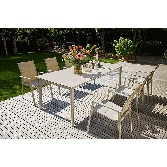 Sunfun Solo Gartentisch - L x B x H: 230 x 100 x 76,5 cm, Aluminium, Sintered Stone, Light-Greige, Ausziehbar - Ein einladender Gartentisch mit Stühlen auf einer Holzterrasse, dekoriert mit Blumen und Geschirr für ein entspanntes Essen im Freien.