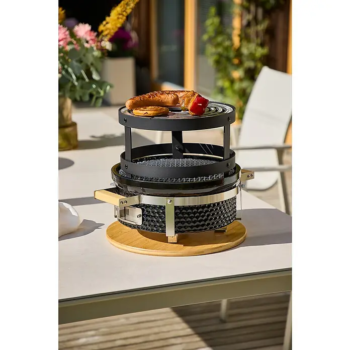 Kingstone Barbacoa de carbón Kamado Barbacoa de mesa - Diámetro de la superficie de la parrilla: 29,5 cm, Negro - Primer plano de una parrilla de mesa moderna con salchichas y kebab en una terraza.