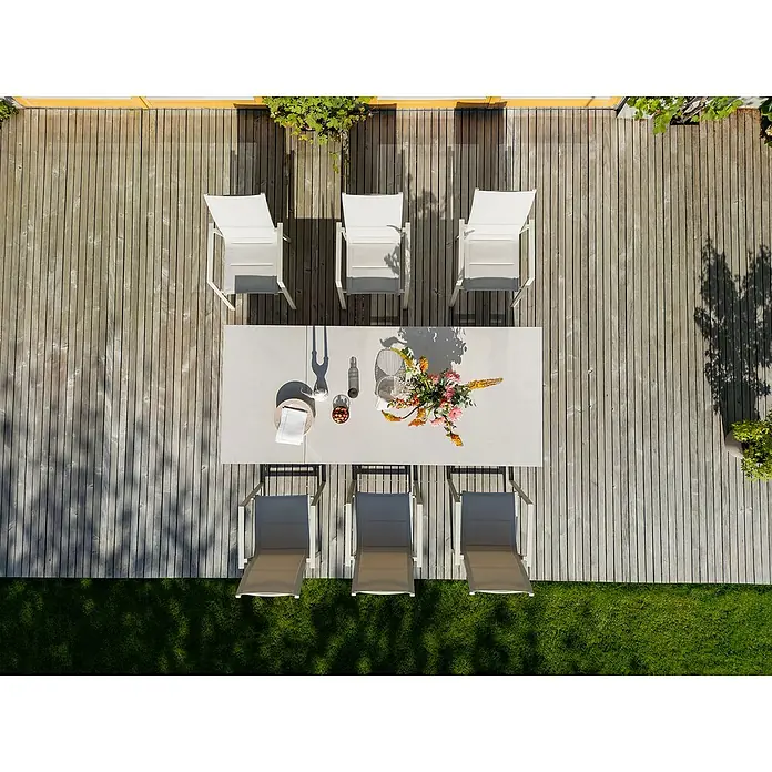 Sunfun Solo Gartentisch - L x B x H: 230 x 100 x 76,5 cm, Aluminium, Sintered Stone, Light-Greige, Ausziehbar - Draufsicht auf einen Gartentisch mit Stühlen auf einer Holzterrasse, dekoriert mit Blumen und Geschirr für eine Mahlzeit im Freien.