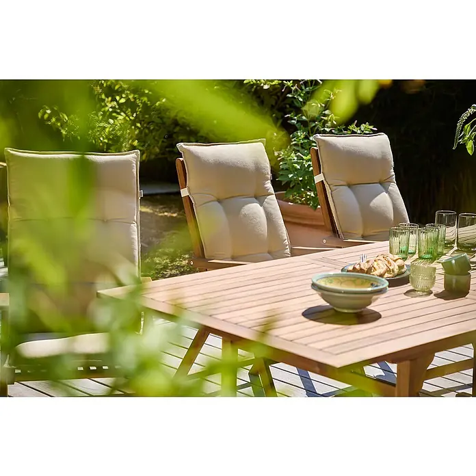 Sunfun Gartenmöbel-Set Diana - 7 -tlg., Akazie, Beige/Braun - Detailaufnahme von Gartenmöbeln mit hellen Polstern und einem Holztisch, der mit Geschirr und Speisen für ein Essen im Freien gedeckt ist.