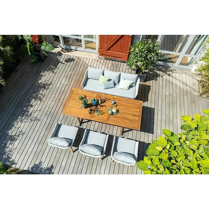 Sunfun Diana Gartentisch - L x B x H: 180 x 100 x 75 cm, Akazie, Naturbraun, Ausziehbar - Einladende Gartensitzgruppe mit einem Holztisch, einem Sofa und Stühlen mit hellgrauen Polstern auf einer Holzterrasse.