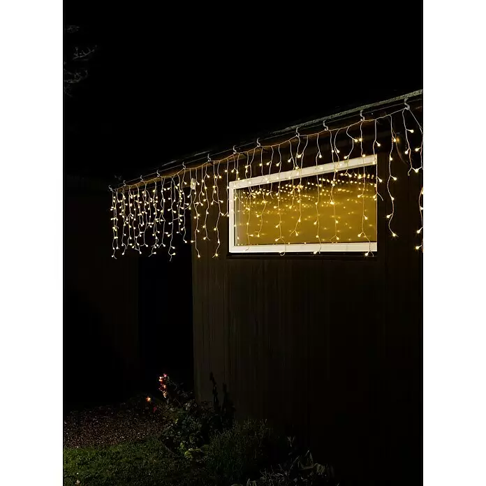 Konstsmide LED-Lichtervorhang Eisregen - Außen, 20,27 m, Warmweiß, 400 Stk., Netzbetrieben - Warmweiße Eiszapfen-Lichterkette beleuchtet eine Dachlinie bei Nacht, mit Reflexionen im Fenster.