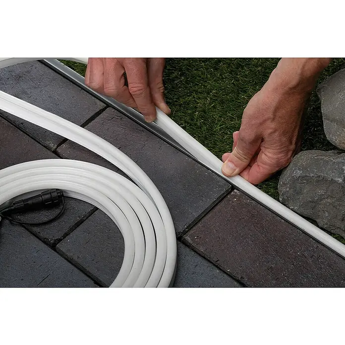 Paulmann Plug & Shine LED-Band Smooth Stripe Outdoor - Länge: 10 m, Lichtfarbe: Warmweiß, 1.540 lm, 24 V, 46 W - Eine Person installiert eine LED-Lichterschlauch neben Pflastersteinen, um einen Gartenweg zu beleuchten. Die LED-Schlauchleuchte sorgt für stimmungsvolle Aussenbeleuchtung.