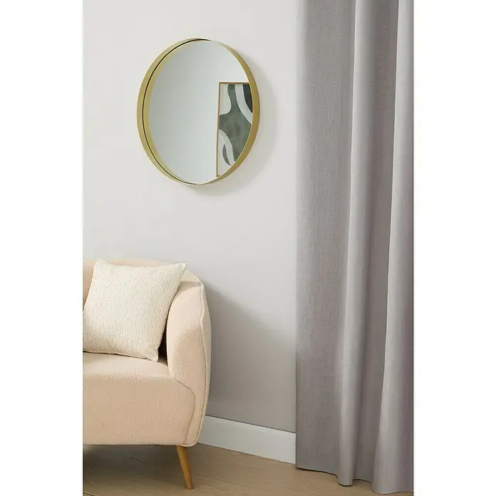 Espejo de pared Gia con marco - Diámetro: 60 cm, Oro - Interior elegante con cortina gris, espejo redondo y sillón beige con cojín. Acogedor espacio habitable.