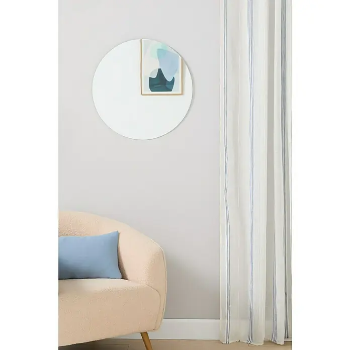 Espejo de pared Gia sin marco - Diámetro: 60 cm, Plateado - Un interior que muestra un espejo redondo en la pared, un sillón rosa con un cojín azul y cortinas blancas con rayas azules.