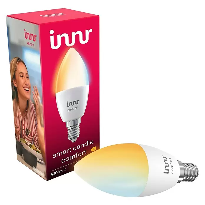 Innr Lighting Smart-LED-Lampe Candle Comfort - E14, Dimmbar, Kaltweiß, 520 lm, 4,6 W, 1 Stk. - Innr Smart Candle Comfort LED-Lampe (E14) in Weiß mit warmgelbem Licht, neben der rot-weißen Produktverpackung.
