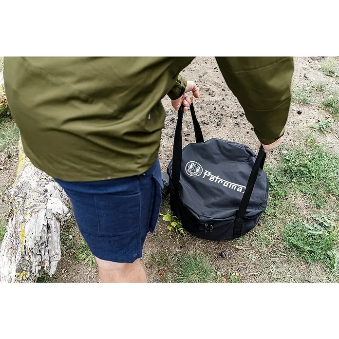 Petromax Transporttasche FT 12 - Ø x H: 45 x 24 cm, Polyester - Eine Person trägt eine schwarze Petromax-Tasche im Freien. Die robuste Tasche mit Tragegurten ist ideal für den Transport von Campingausrüstung.