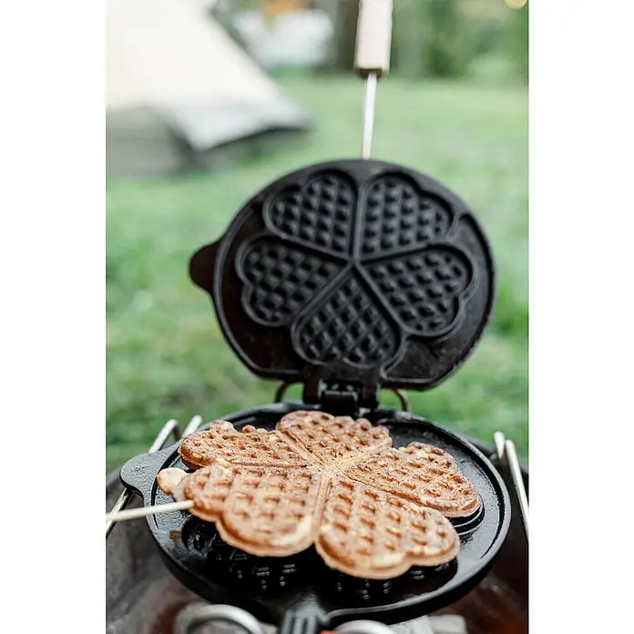 Petromax Waffeleisen zum Wenden - L x B: 54 x 22 cm, Gusseisen - Herzförmige Waffel in einem gusseisernen Waffeleisen über einem Campingkocher zubereitet, mit einem Zelt im Hintergrund.