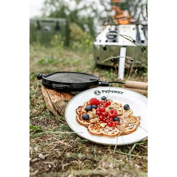 Petromax Teller rund - Ø x H: 22,5 x 2,5 cm, Weiß, Stahl, 2 Stk. - Ein Teller Petromax-Waffeln mit Beeren und eine Waffelpfanne im Hintergrund. Perfekt für ein leckeres Outdoor-Frühstück.