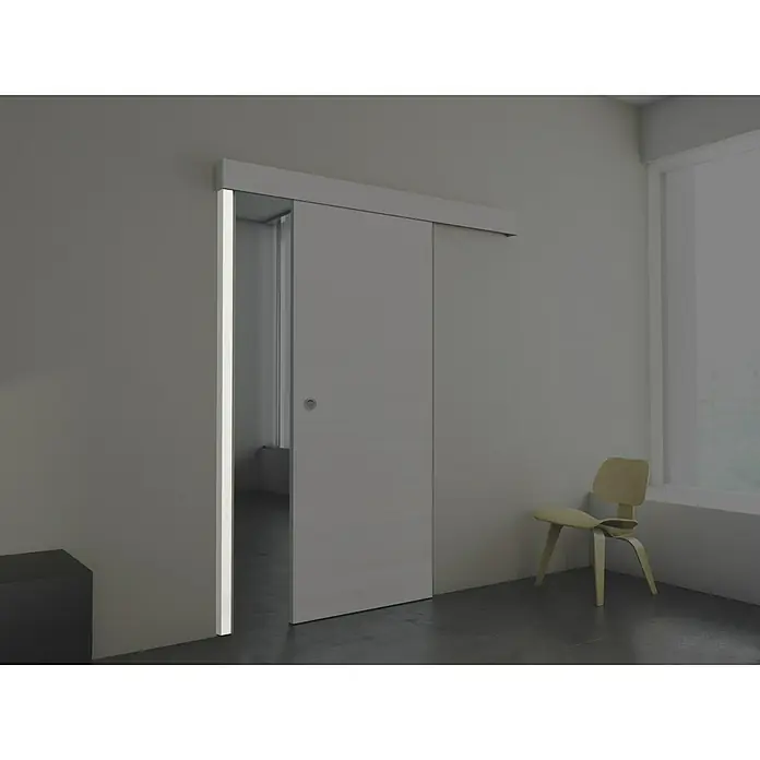 Estructura batiente Fresno Eslovenia - 67 x 2.140 mm, Blanco - Interior moderno con una elegante puerta corredera gris parcialmente abierta, que revela una vista de otra habitación, junto a una silla.