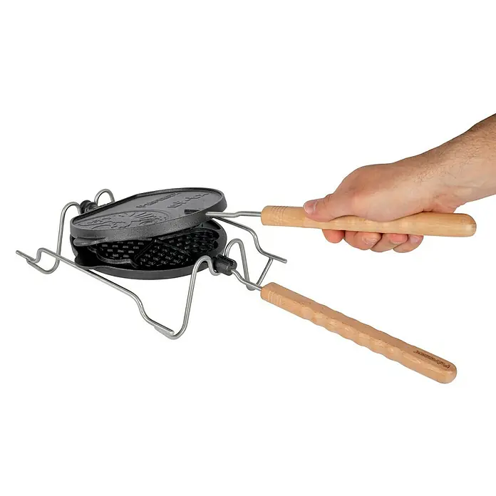 Petromax Waffeleisen zum Wenden - L x B: 54 x 22 cm, Gusseisen - Bild einer Sandwichtoaster für Lagerfeuer mit Holzgriffen, der von einer Hand gehalten wird, auf schwarzem Hintergrund.