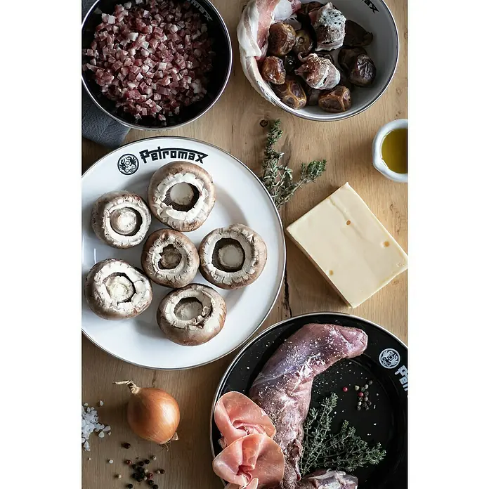Petromax Teller rund - Ø x H: 22,5 x 2,5 cm, Weiß, Stahl, 2 Stk. - Draufsicht auf eine Auswahl von Kochzutaten, darunter Pilze, Fleisch, Käse und Kräuter, arrangiert auf Holztischen und in Petromax Schalen.
