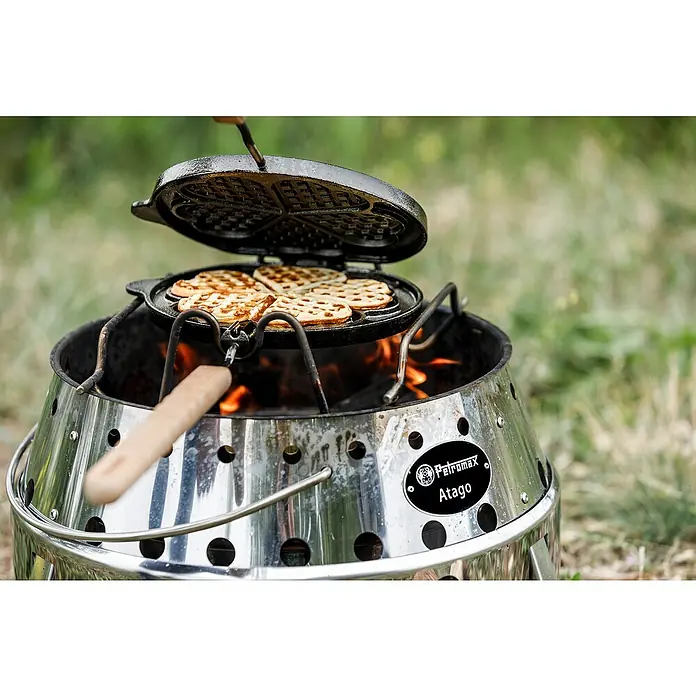 Petromax Waffeleisen zum Wenden - L x B: 54 x 22 cm, Gusseisen - Herzförmige Waffeln werden mit einem Petromax Atago auf einem Grill zubereitet, was ein gemütliches kulinarisches Erlebnis im Freien ermöglicht.