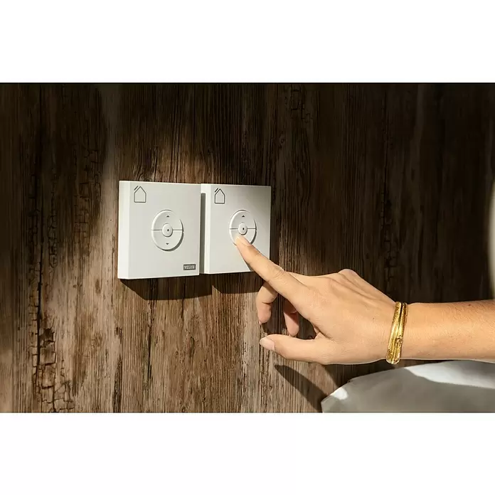 Velux Funk-Wandschalter Hitzeschutz KLI 313 - Passend für: Außen liegende VELUX Solar-/Elektro-Rollläden und -Markisen (io-homecontrol®) - Zwei weiße Velux-Bedienfelder an einer Holzwand, eines wird von einer Hand gedrückt. Mit Richtungs- und Home-Tasten.