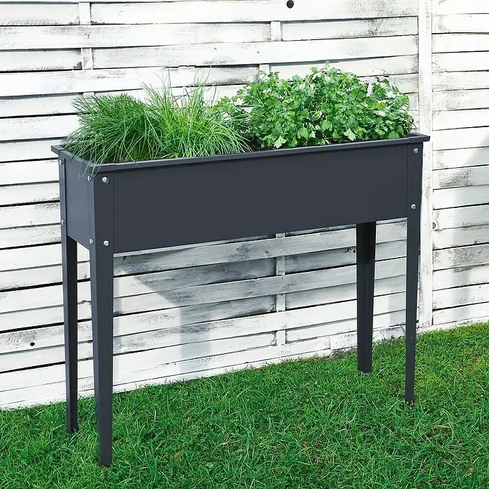 Floraworld Hochbeet - 80 x 100 x 30 cm, Metall, Anthrazit - Ein erhöhter, grauer Pflanzkasten mit grünen Pflanzen steht vor einem weißen Holzzaun auf Rasen.