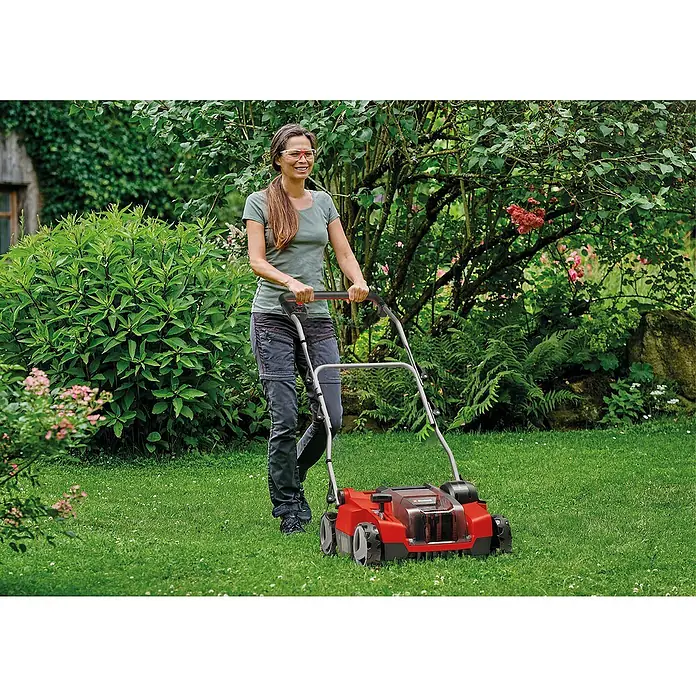 Einhell Power X-Change 18V Akku-Vertikutierer-Lüfter GE-SC 36/35 LI SOLO - Anzahl Akkus: Ohne Akku, 36 V - Frau benutzt einen roten Vertikutierer im Garten. Das Gerät hilft dabei, den Rasen gesund und grün zu halten.