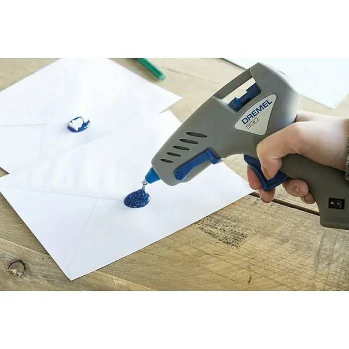 Dremel Pistola termoencoladora Hobby 930-18 - Diámetro cartucho de cola: 7 mm, Tiempo de calentamiento: 5 min - La pistola de pegamento Dremel 930 se está utilizando para sellar cartas con cera azul sobre una mesa de madera.