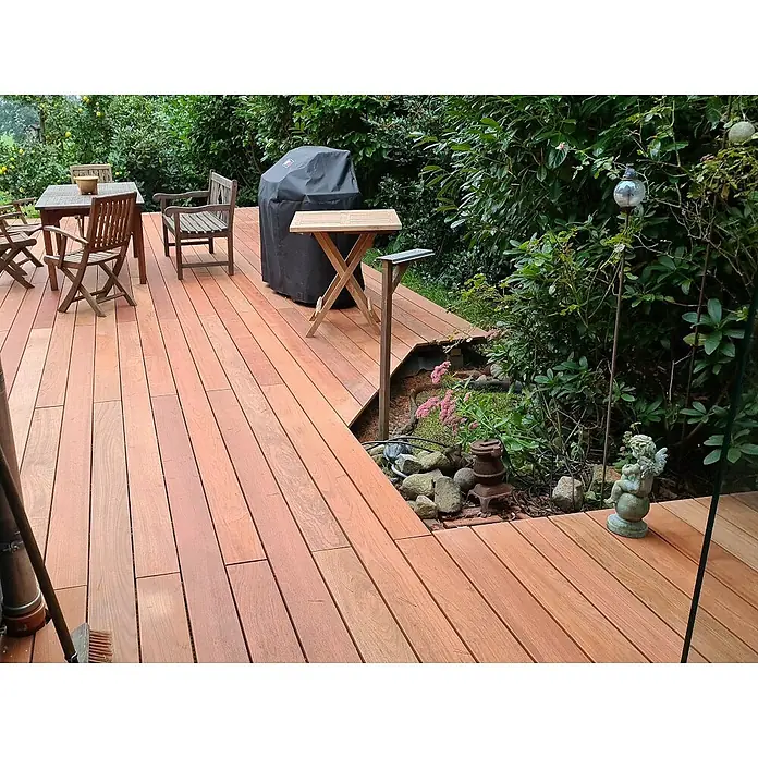 Terrassendiele - 244 x 14,5 x 2,1 cm, Braun - Blick auf eine Holzterrasse mit Gartenmöbeln und Grill, umgeben von üppigem Grün, die zum Verweilen einlädt.