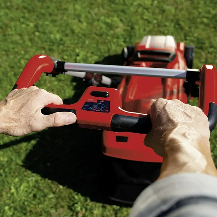 Einhell Power X-Change 18V Akku-Rasenmäher GE-CM 36/37 Li-Solo - 18 V, Ohne Akku, Schnittbreite: 37 cm - Hände schieben einen roten Rasenmäher über einen grünen Rasen. Der Rasenmäher ist mit einem Sicherheitsetikett versehen.
