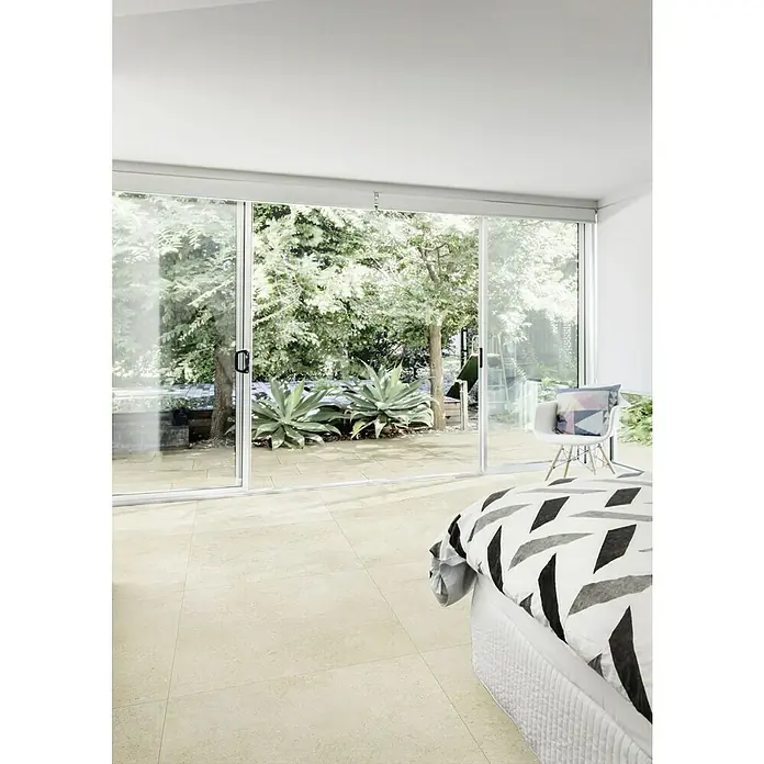 Marazzi Feinsteinzeugfliese Jerusalem Oase Avorio - 75 x 75 cm, Sandstein-Beige, Matt - Elegantes Schlafzimmer mit beigem Fliesenboden, der durch die Schiebetür einen nahtlosen Übergang zum Garten bietet. Helle, offene Raumgestaltung.