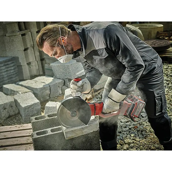 Einhell Professional Power X-Change 18V Akku-Winkelschleifer Axxio 36/230 Q - 18 V, Ohne Akku, Durchmesser Scheibe: 230 mm - Mann schneidet Stein mit einem Trennschleifer. Persönliche Schutzausrüstung wie Schutzbrille und Atemschutzmaske werden getragen.