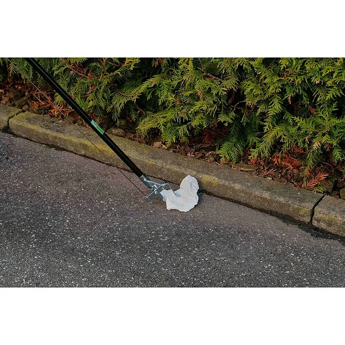 Freund Victoria Greifzange - Länge: 87 cm, Aluminium - Müllsammler mit Greifzange hebt ein weißes Papiertuch vom Straßenrand auf, Busch im Hintergrund.