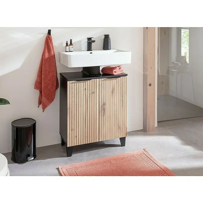 Riva Badmöbel-Set Rigato - 61 cm, Eiche/Schwarz, Strukturiert, 3 -tlg. - Ein Badezimmerwaschtisch mit Waschbecken, Armatur, Handtuch und schwarzem Mülleimer. Der Waschtisch hat eine Holzfront und einen schwarzen Rahmen.