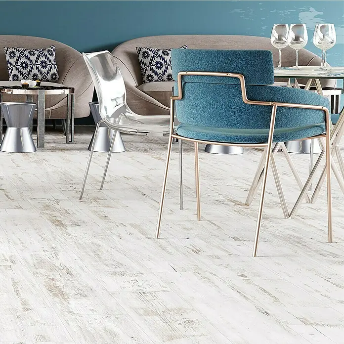 Feinsteinzeugfliese Natura - 22,5 x 90,2 cm, Shabby White, Matt - Elegantes Interieur mit einem stilvollen blauen Sessel mit goldenem Gestell und einem transparenten Stuhl auf einem hellen Holzboden.