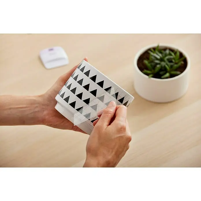 Cricut Vinylfolie Material Starter Bundle - 9 -tlg., Bunt - Eine Person bringt eine schwarze Dreiecksfolie auf einen weißen Pflanztopf an, um ihn zu dekorieren.