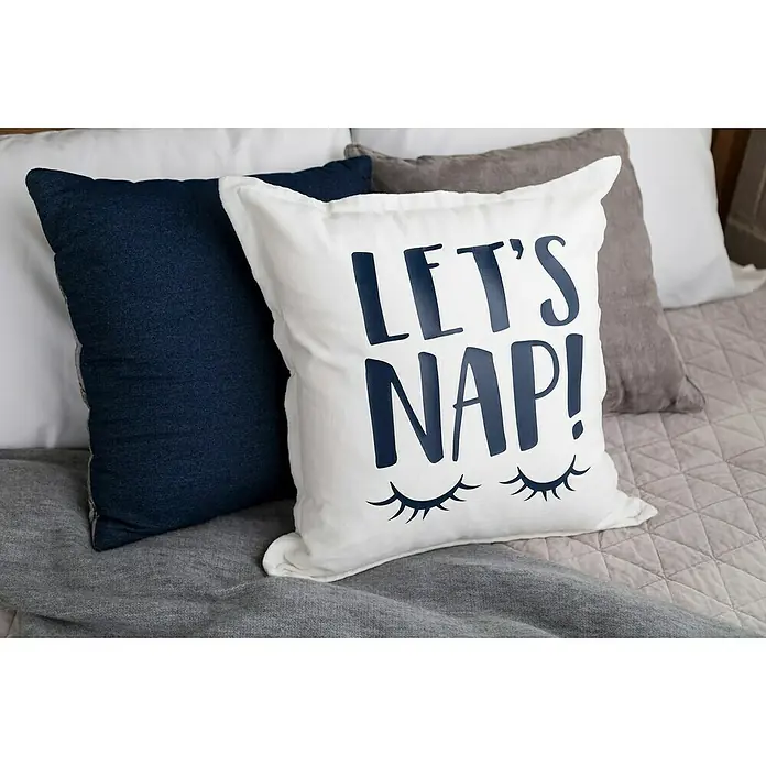 Cricut Vinylfolie Material Starter Bundle - 9 -tlg., Bunt - Dekorative Kissen auf einem Bett, darunter ein weißes Kissen mit der Aufschrift "Let's Nap!" und einem Augendesign für einen erholsamen Schlaf.