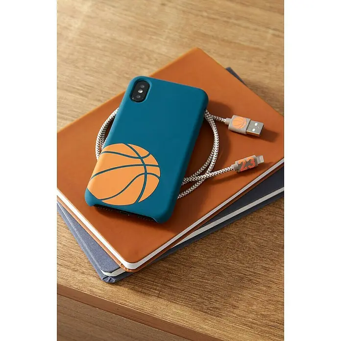 Cricut Vinylfolie Material Starter Bundle - 9 -tlg., Bunt - Das blaue Handycase mit Basketball-Motiv und passendes Ladekabel auf einem Notizbuch, ideal für Sportfans.