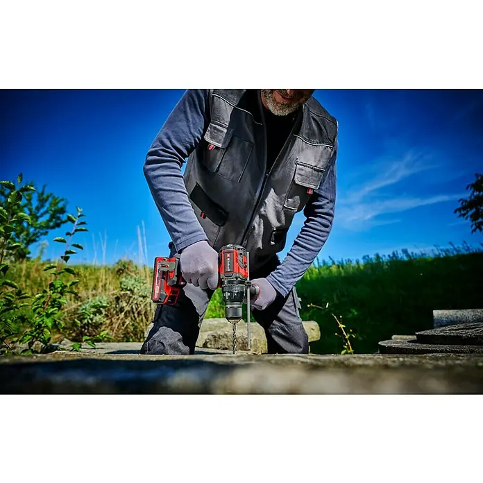 Einhell Professional PXC 18V Taladro atornillador percutor de batería TP-CD 18/120 Li-i BL - Solo - 18 V, Sin batería, 120 Nm - Un hombre está taladrando un agujero en una piedra con un taladro inalámbrico Einhell. El taladro es rojo y negro.