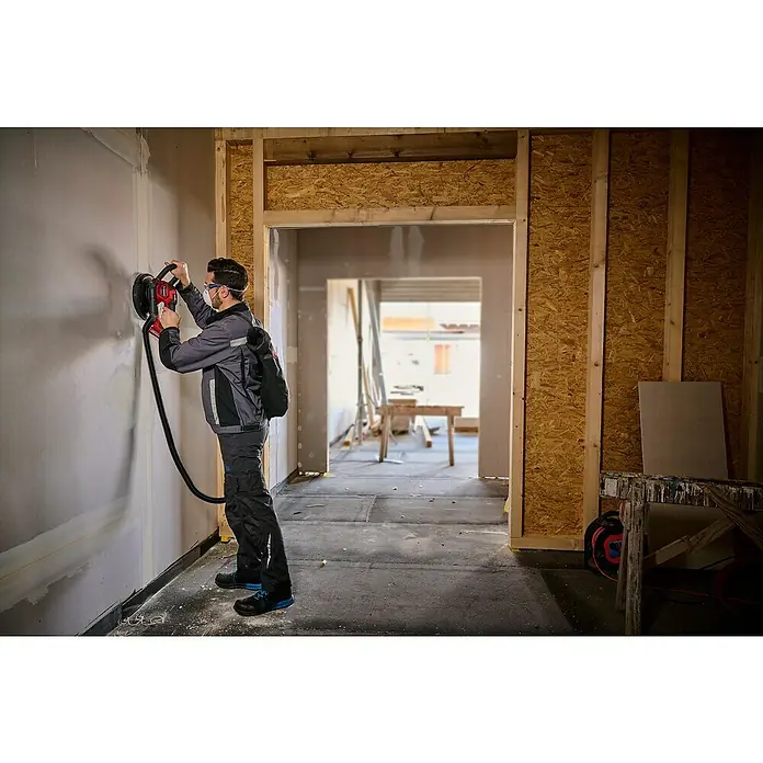 Einhell Professional Power X-Change 18V Akku-Trockenbauschleifer TP-DWS 18/225 Li BL Solo - 18 V, Ohne Akku - Ein Handwerker verwendet einen elektrischen Wandschleifer von Einhell, um eine Wand in einem Rohbau zu bearbeiten.