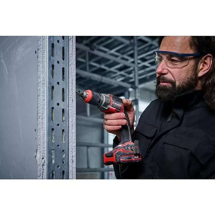 Einhell Professional PXC 18V Atornillador para placas de yeso de batería TP-DY 18 Li BL - Solo - 18 V, Sin batería, 5.000 r.p.m. - Hombre con equipo de seguridad usa atornillador rojo y negro para fijar placa de yeso a estructura metálica.