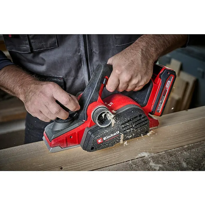 Einhell Power X-Change 18V Akku-Hobel TP-PL 18/3 LI BL - Solo - 18 V, Ohne Akku, Hobeltiefe: 3 mm, 12.000 U/min - Der Einhell Akku-Hobel wird auf einem Holzbrett benutzt. Der Hobel ist rot und schwarz und hat einen Akku. Holzspäne fliegen durch die Luft.
