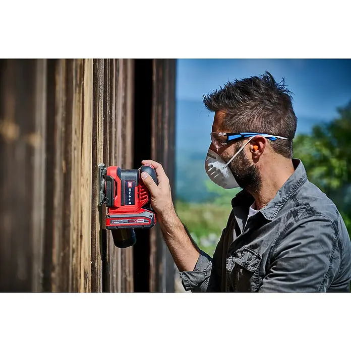 Einhell Power X-Change 18V Akku-Schwingschleifer TE-OS 18/113 3X LI - 18 V, Ohne Akku - Ein Mann verwendet einen Einhell Akku-Multischleifer zum Abschleifen einer Holzwand, mit Schutzbrille und Maske für zusätzliche Sicherheit.
