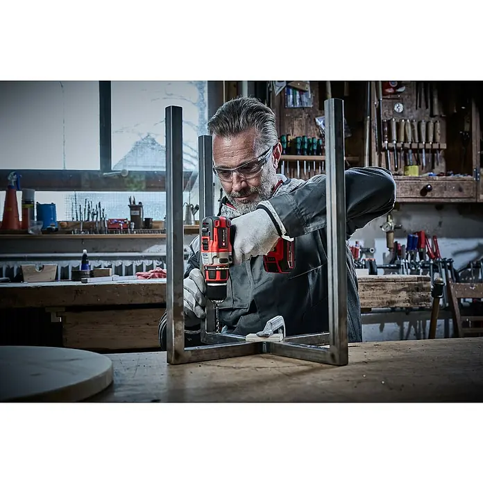 Einhell Professional Power X-Change 18V Akku-Bohrschrauber TP-CD 18/80 LI BL-Solo - 18 V, Ohne Akku, 80 Nm - Ein Mann, der mit einer roten Einhell Akku-Bohrmaschine an einem Metallrahmen arbeitet, geschützt mit Handschuhen und Brille.