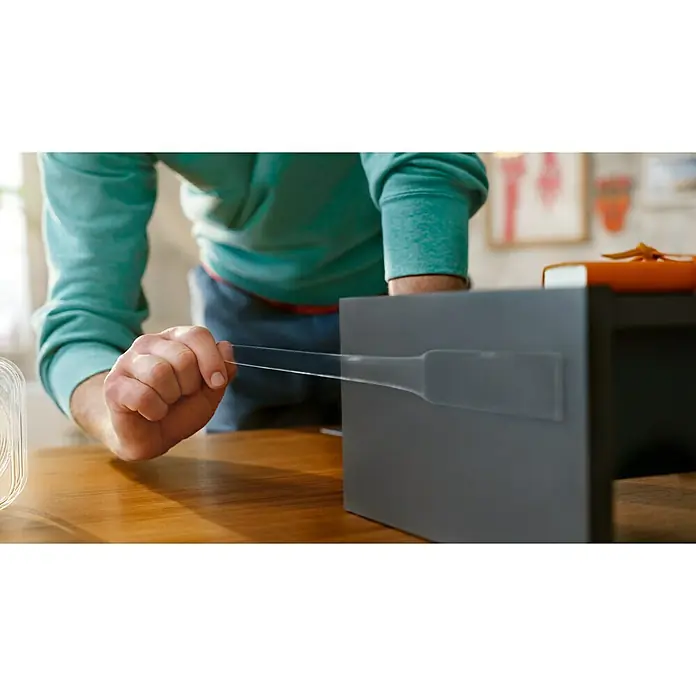 Tesa Doppelseitiges Klebeband Universal Tape with Nano Power - 3 m x 30 mm - Ein Mann befestigt mit klarem Klebeband eine graue Box auf einer hölzernen Tischoberfläche. Die Box ist Teil eines größeren DIY-Projekts.