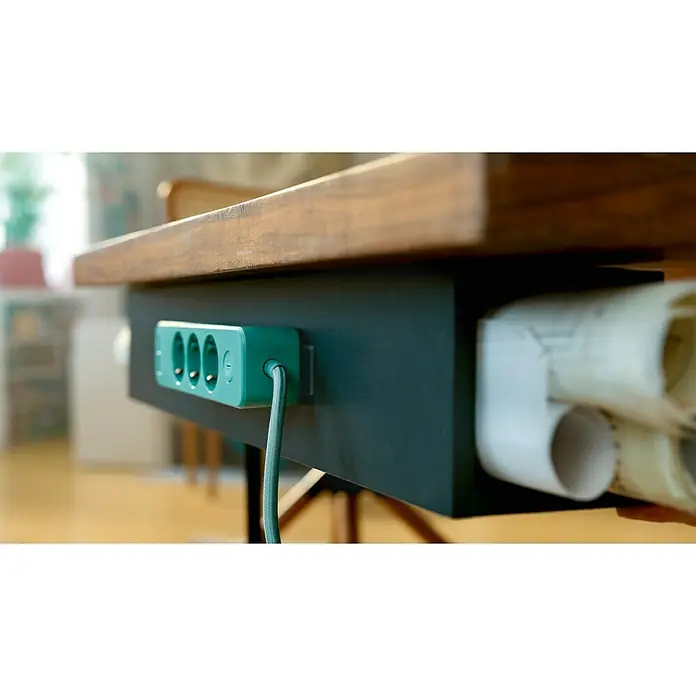 Tesa Doppelseitiges Klebeband Universal Tape with Nano Power - 3 m x 30 mm - Nahaufnahme einer mintgrünen Steckdosenleiste, die unter einer hölzernen Tischplatte befestigt ist und ein modernes und praktisches Design zeigt.
