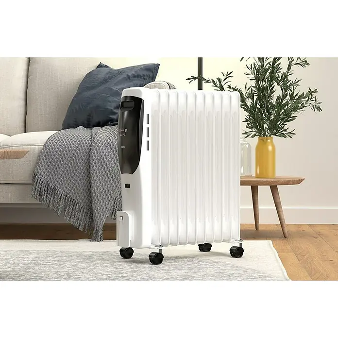 Rointe Radiador de aceite Lorent - 2.500 W, Blanco/Negro, 15 x 50 x 58 cm - Un radiador de aceite blanco con controles negros se encuentra sobre una alfombra estampada frente a un sofá y una mesa auxiliar.