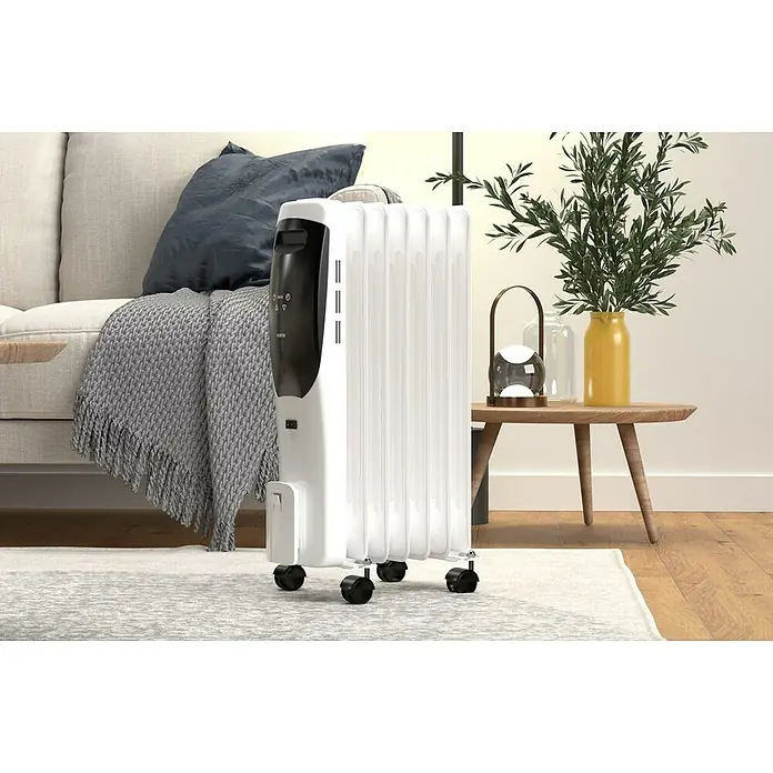 Rointe Radiador de aceite Lorent - 1.500 W, Blanco/Negro, 15 x 35 x 58 cm - Un radiador de aceite portátil blanco se encuentra sobre una alfombra estampada frente a un sofá y una mesa auxiliar en la sala de estar.