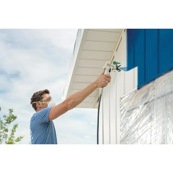 Wagner High Efficiency Airless Farbsprühsystem Control 150 M - 350 W, Förderleistung: 0,9 l/min - Ein Mann, der mit einer Farbspritzpistole eine blaue Wand streicht, wobei er eine Schutzmaske und eine Schutzbrille trägt.