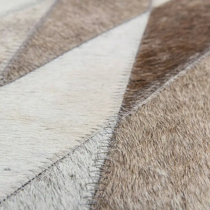 Kayoom Lederteppich Eclipse 510 - Grau/Braun/Beige, 150 x 80 cm, 100 % Leder - Nahaufnahme eines Kuhfellteppichs mit geometrischen Formen in Weiß- und Brauntönen, der durch dekorative Ziernähte verbunden ist.